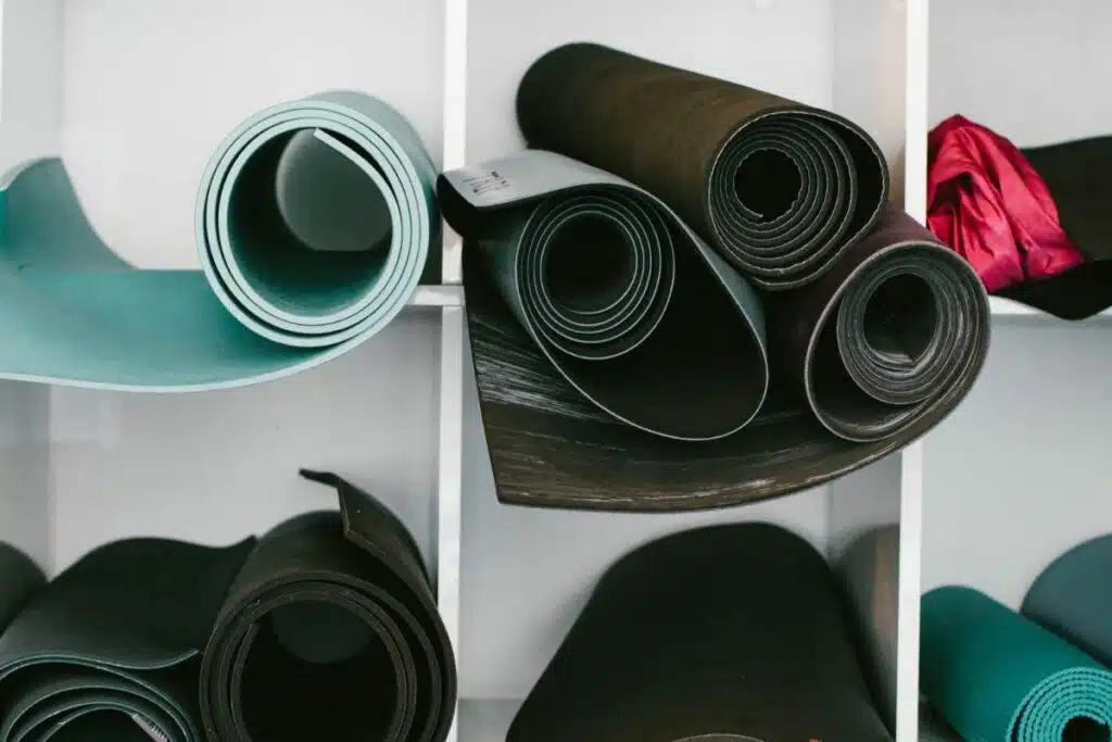 Image of several yoga mats neatly rolled and arranged in a variety of colors, suggesting a readiness for a group yoga session or a selection of mats for personal use.