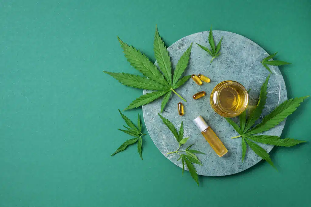 CBD oil, hemp oil capsules and cannabis leaves on green background. Flat lay, copy space. Cosmetics CBD oil. Alternative medicine. Natural supplements, treatment.