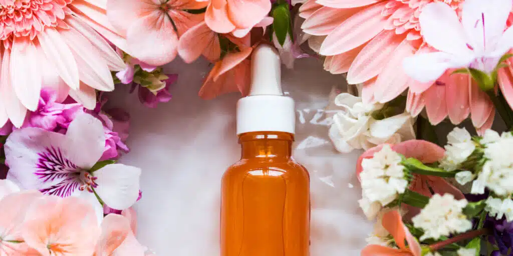 Skin care serum in orange bottle with dropper with beautiful flowers around. Natural beauty product