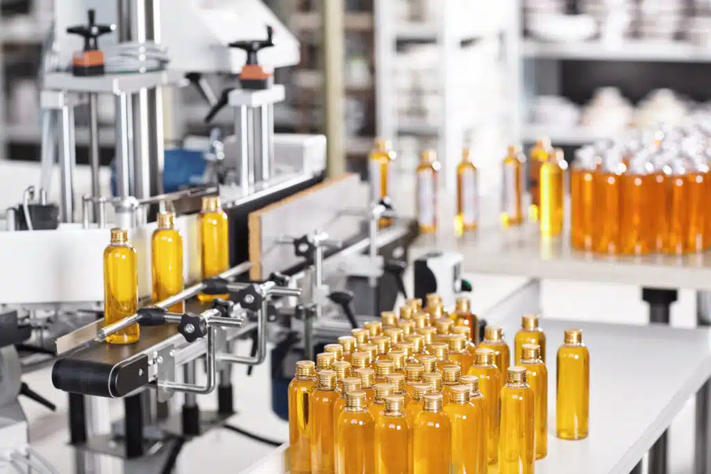 Bottles filled with yellow thick substance standing on desk and conveyor line. Production line of cosmetics products on big factory.Automated process of creation shampoo on factory.Research concept white label 