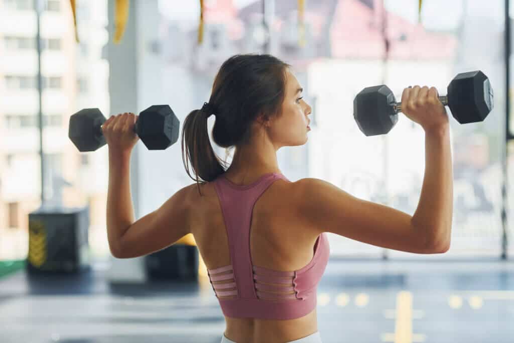 Doing exercises by using weights. Beautiful young woman with slim body type is in the gym.