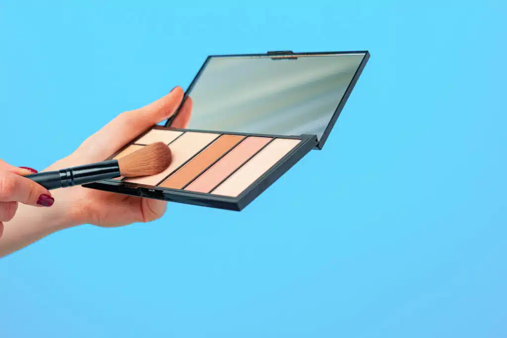 Female hand holding cosmetic palette against blue background close up