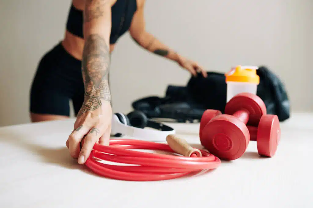 Cropped image of fit woman packing gym bag and putting skippinig rope, dumbbells and headphones inside
