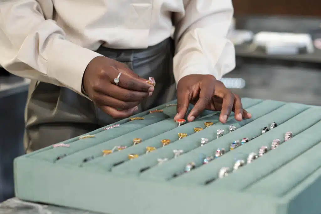 Hands of young African shop assistant helping client of luxurious jewelry boutique with choice of engagement ring