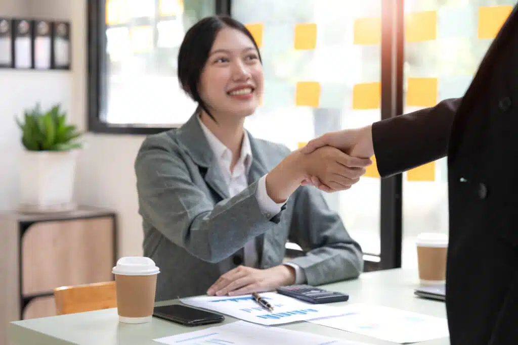 Two Asian small business private label businesswomen are shaking hands in the office. business cooperation, business dealing, Congratulations, greeting. close-up hands image.