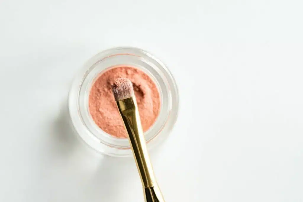 Close-up image of a pan of pinkish eyeshadow, showcasing its texture and shimmer, placed on a neutral background.