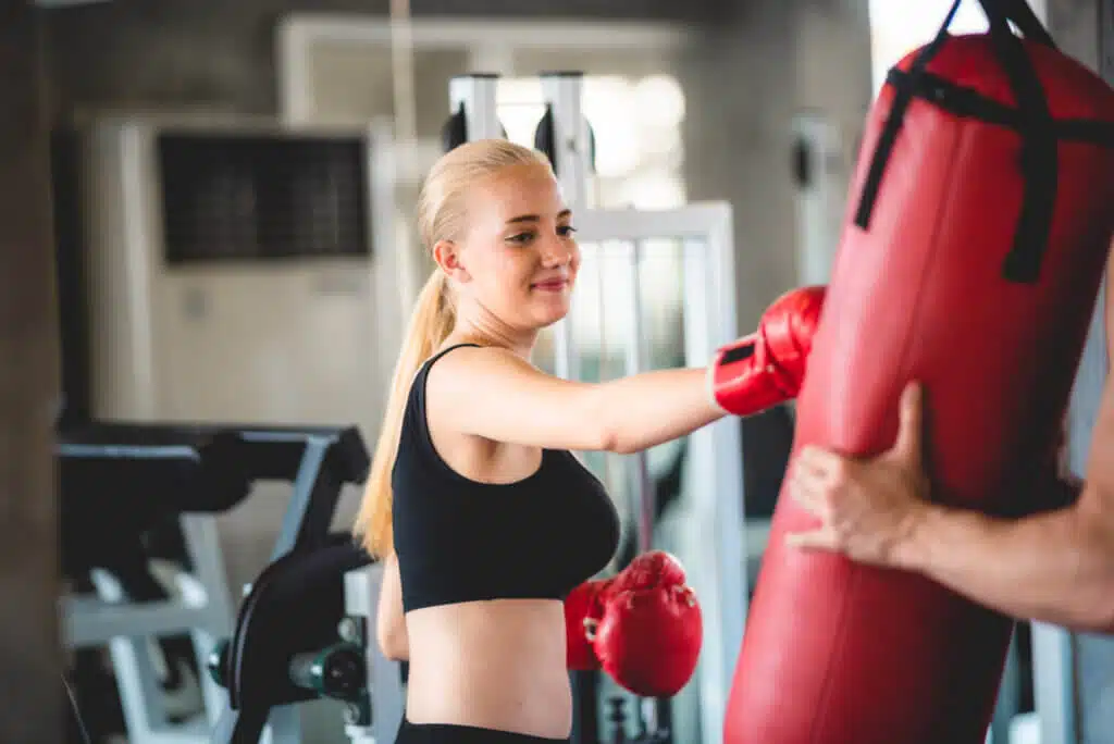 Strong young sportwoman exercising kick boxing and wearing gloves with trainer at fitness brand private label brand 