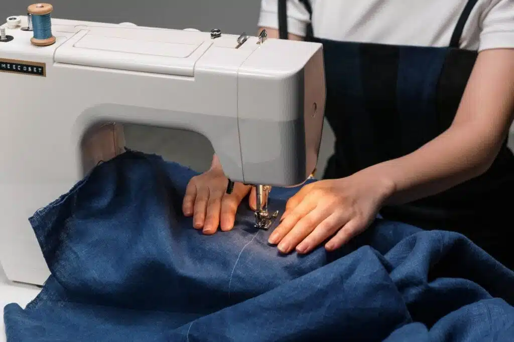 A woman engaged in sewing, focusing on her hands skillfully manipulating fabric through a sewing machine, showcasing craftsmanship and creativity.