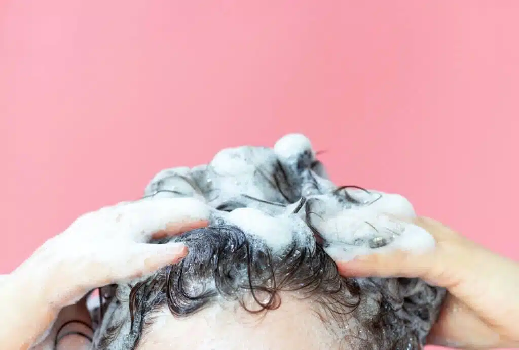 A girl washes her hair with shampoo on a pink background, front view