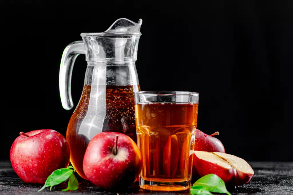 Apple juice in a jug and a glass on the table. On a black background. High quality photo of Beverage Production