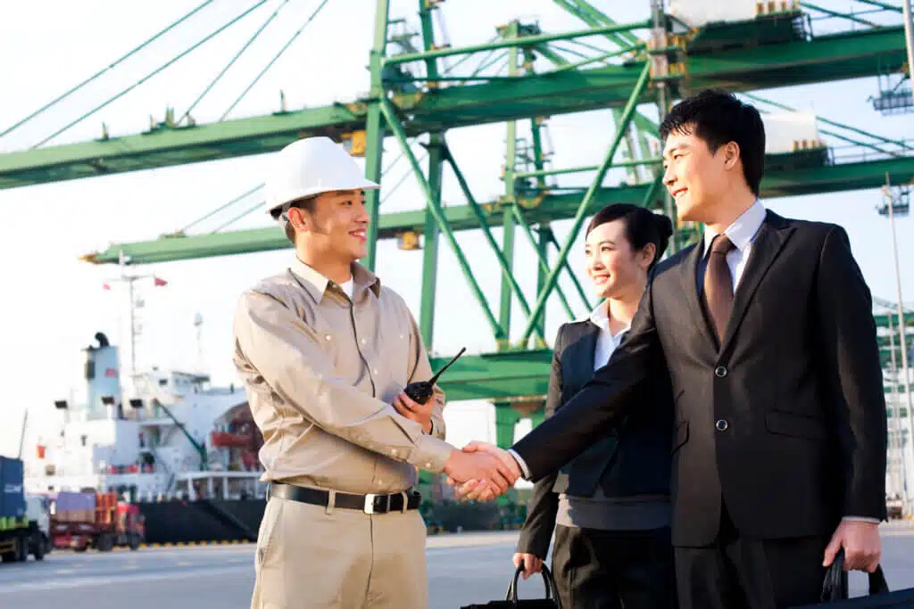 Chinese businesspeople and a shipping industry worker shaking hands at a shipping port