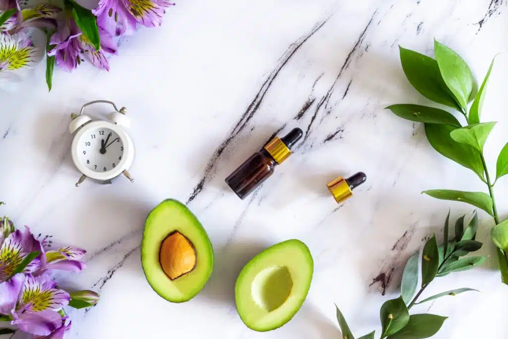 Flat lay composition of natural cosmetics for face skin care, serum and avocado. Top view on a white marble table. Self-love concept, plastic free.
