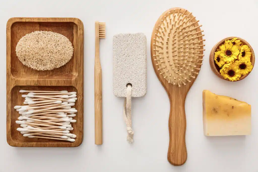 flat lay with wooden dish with cotton swabs and loofah near toothbrush, hairbrush, piece of soap,