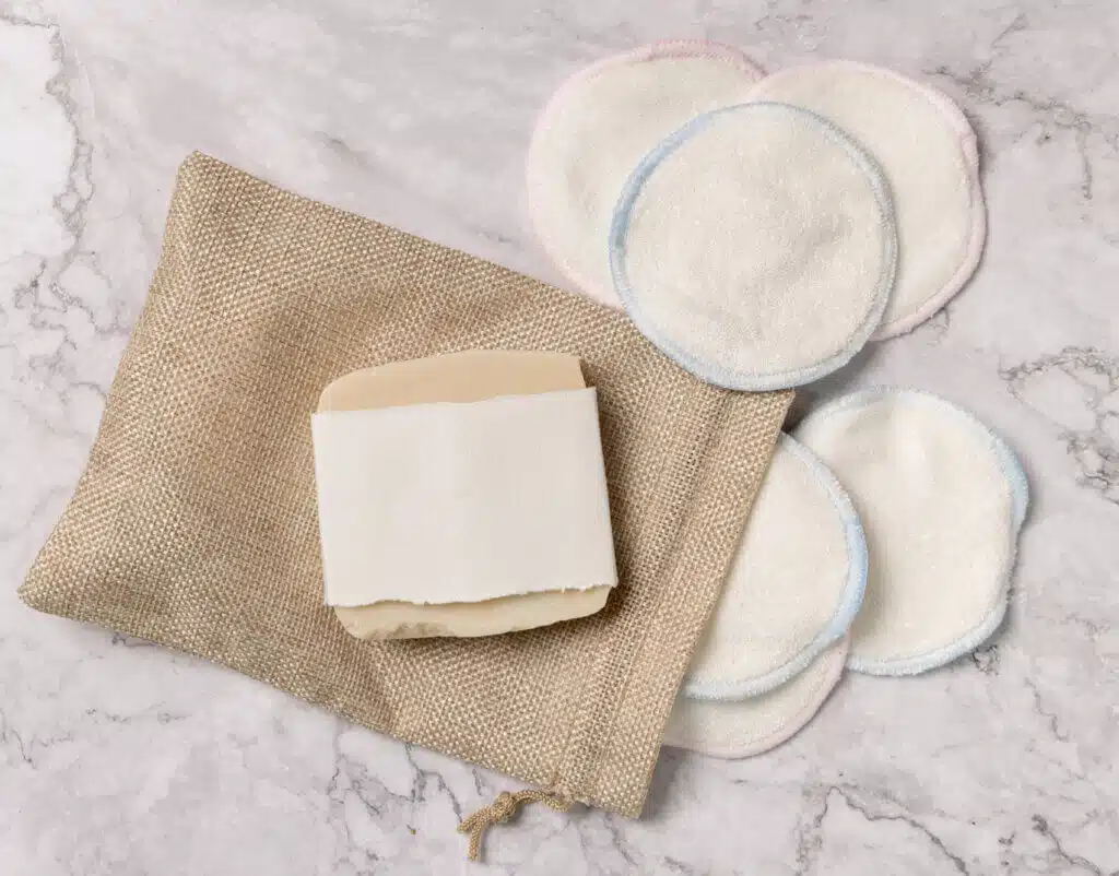 Handmade soap mockup and reusable make-up remover pads with a bag on a white marble top view