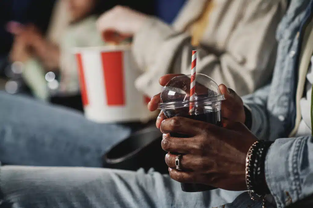 Selective focus shot of unrecognizable Black man holding plastic cup with cola drink at cinema for Beverage Production