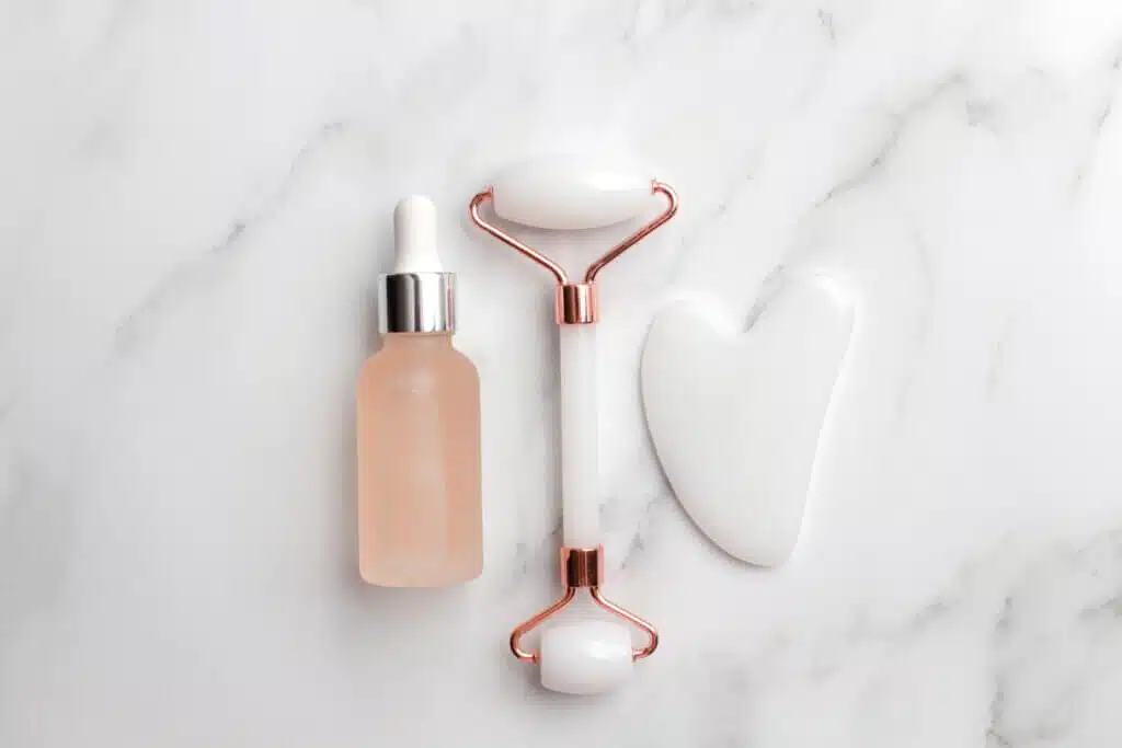 dropper, gua sha and face roller, face yoga tool lined up in marble surface