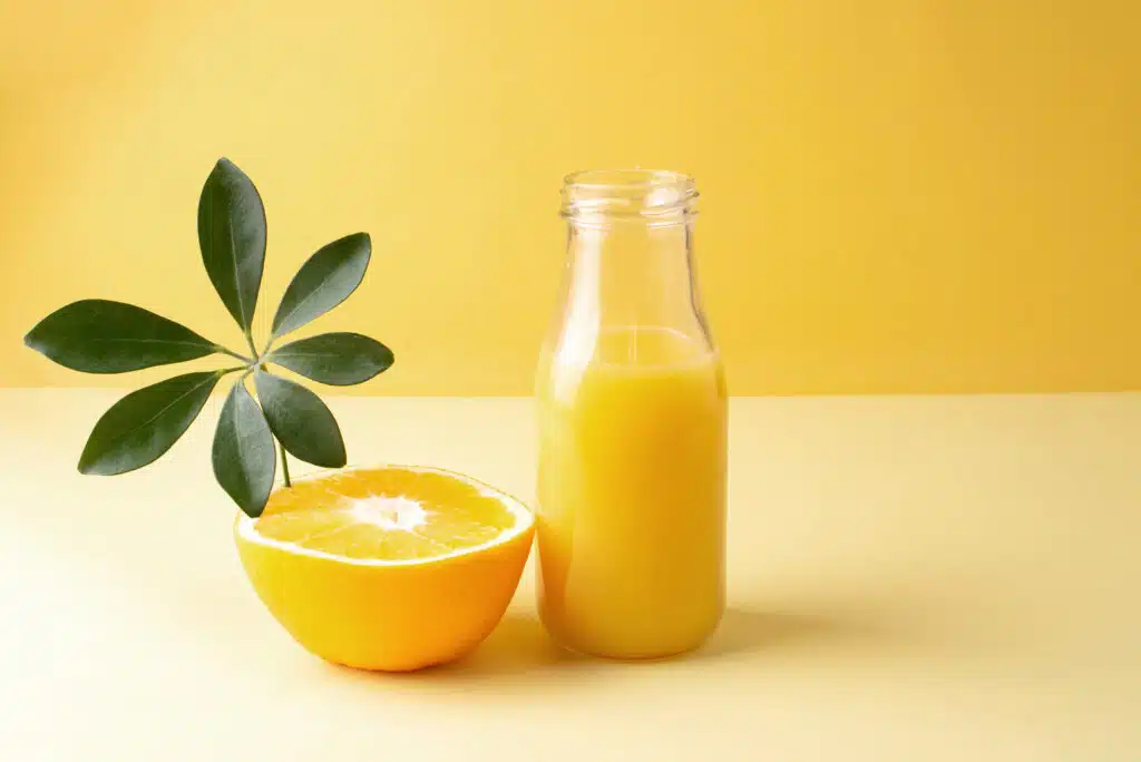 A bottle of fresh orange juice and a half of an orange on a yellow background, close up, copy space for Beverage Production