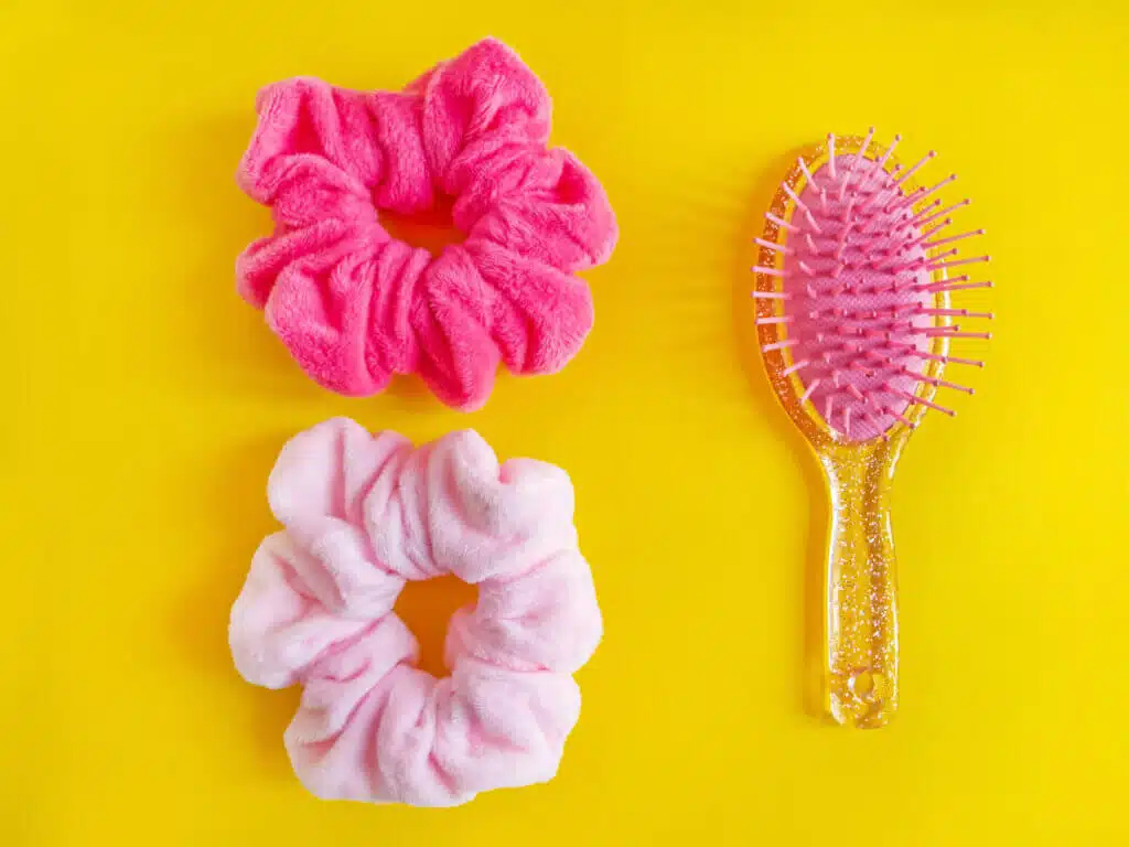 Pink comb and bright spiral scrunchies on the white wooden desk. Bright beauty background with place for text.