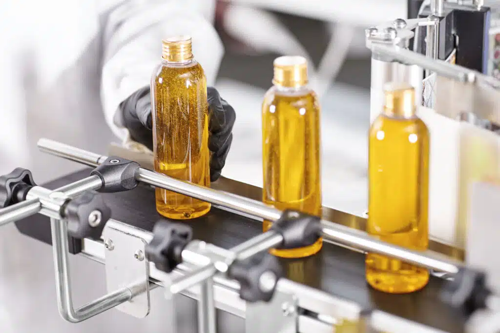 Ready goods on conveyor. Three glass bottles filled with yellow liquid of shampoo ready for transportation standing on manufacturing facility. Trendy shampoo produced by manufactures on factory