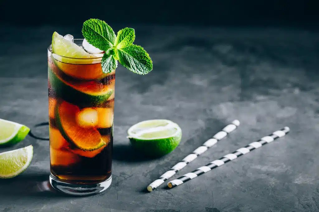 Rum and Cola Cuba Libre ice cold drink cocktail with lime and mint on dark background of Beverage Production