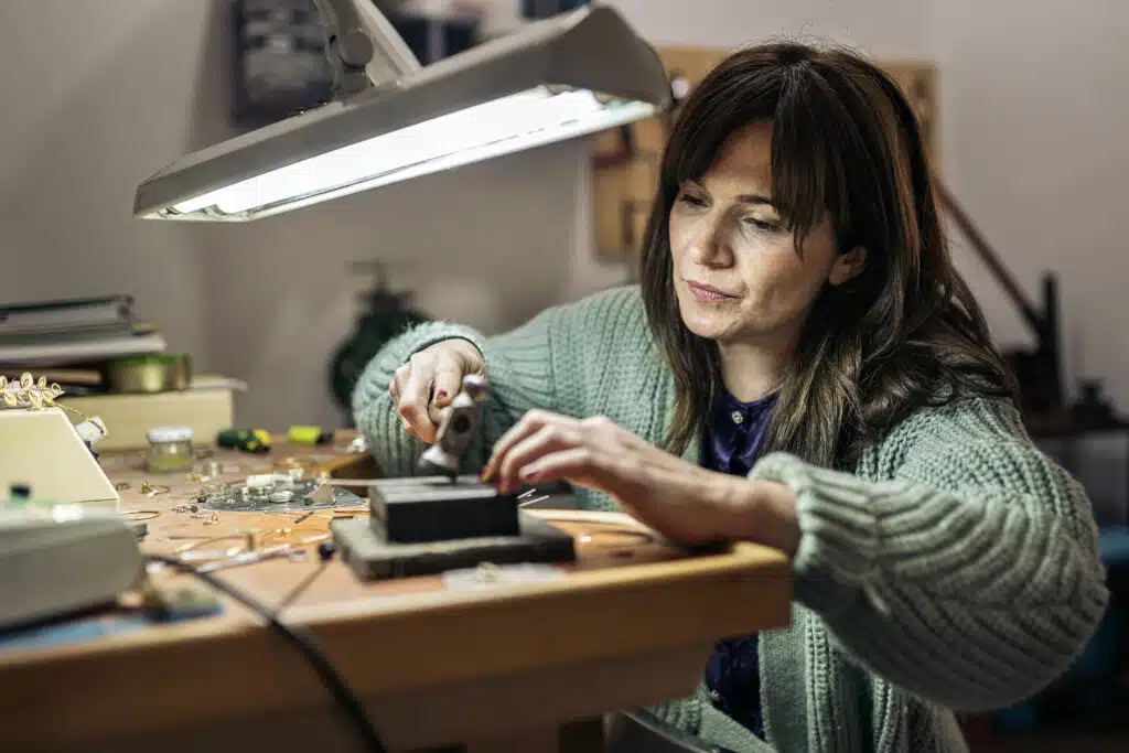 Stock photo of concentrated woman using hammer in jewelry workshop.