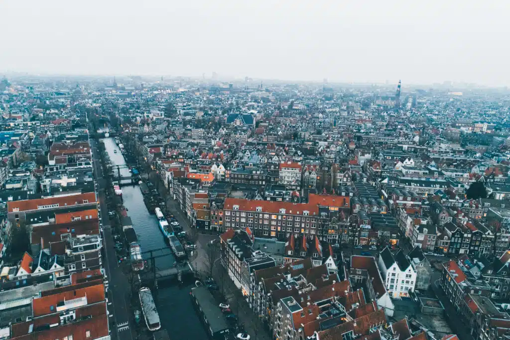 Flying over european city. From above view of old architectural buildings in city infrastructure with light haze above in gloomy day. Amsterdam.