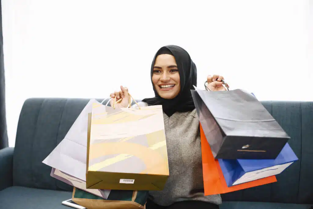 Modern arab girl in hijab at home, doing shopping online, while sitting on couch in living room.. Concept of easy online shopping.