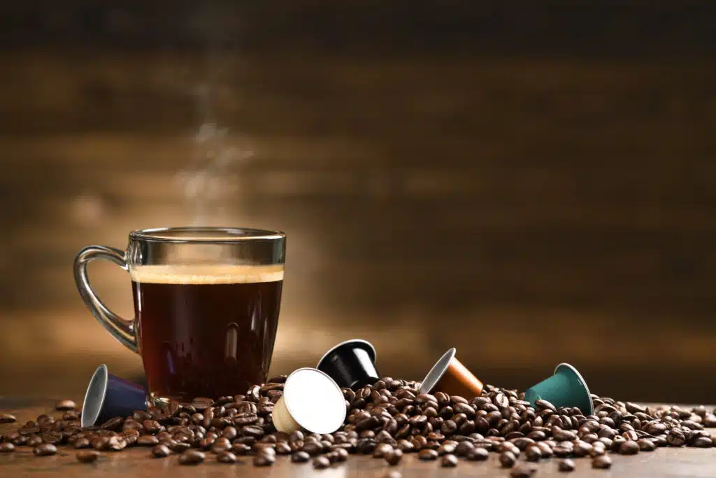 Cup glass of coffee with smoke and coffee beans and coffee capsule on old wooden background