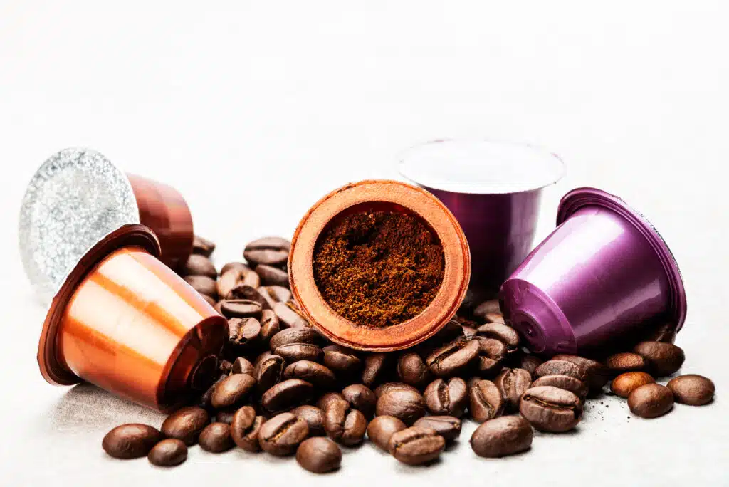 Open Espresso coffee capsule with grounded coffee inside, assorted coffee pods and roasted coffee beans on grey background