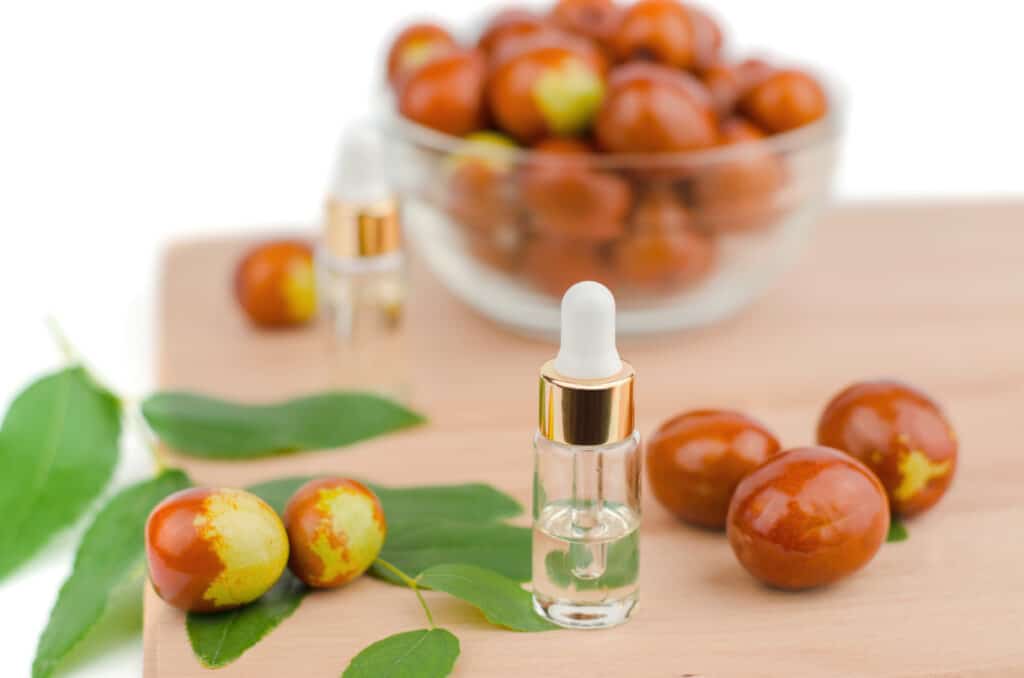 Jojoba oil in a transparent bottle with a dropper and fresh jojoba fruit on a wooden table. Chinese date fruit and oil