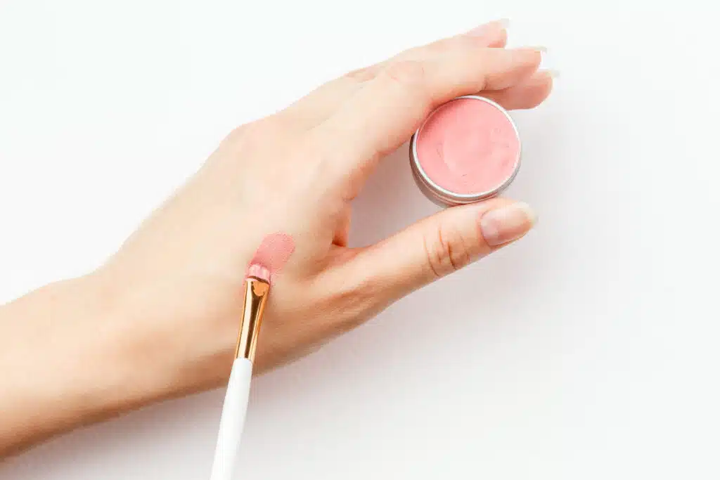 Making a swatch on a female hand of pink nude vegan tinted lipstick or cheek blush in refillable eco-friendly metal packaging
