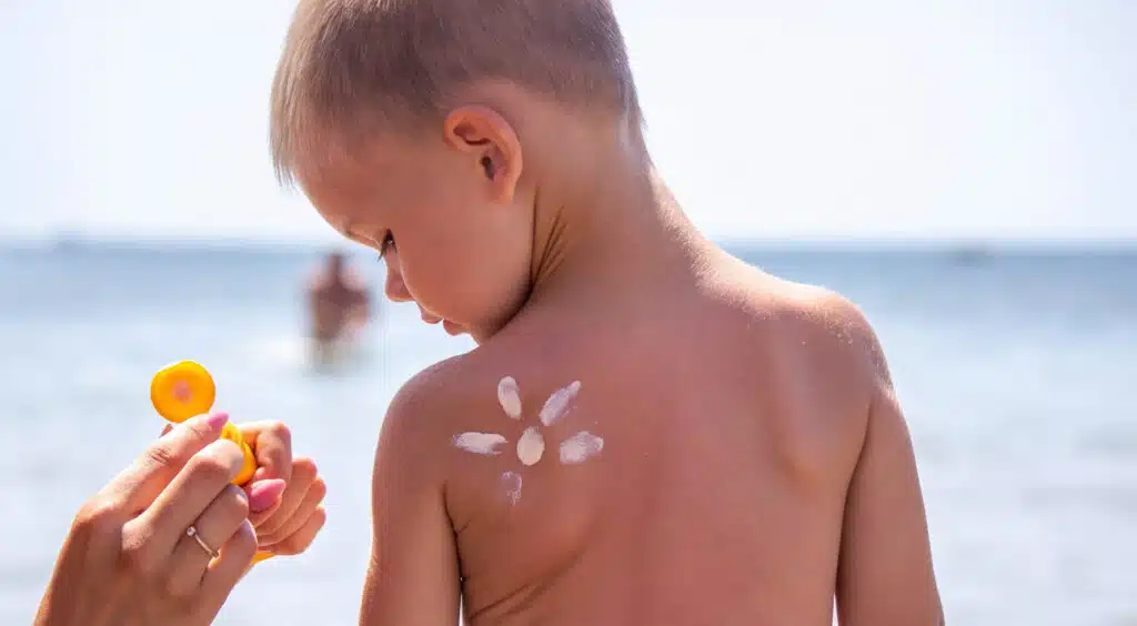 Sunscreen on the child's face and back. On the background of the sea. Selective focus