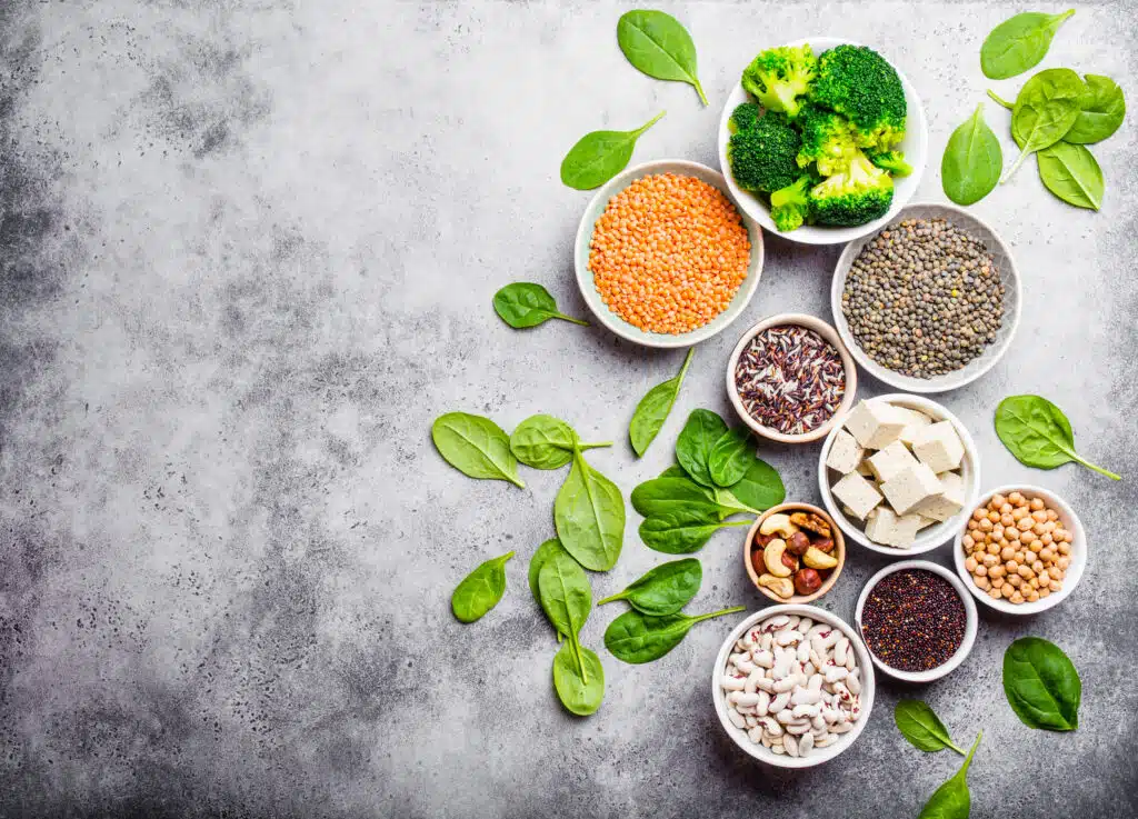 Top view of different vegan protein sources with space for text: beans, lentils, quinoa, tofu, vegetables, nuts, chickpeas, rice, stone background. Healthy balanced vegetarian nutrition for vegans