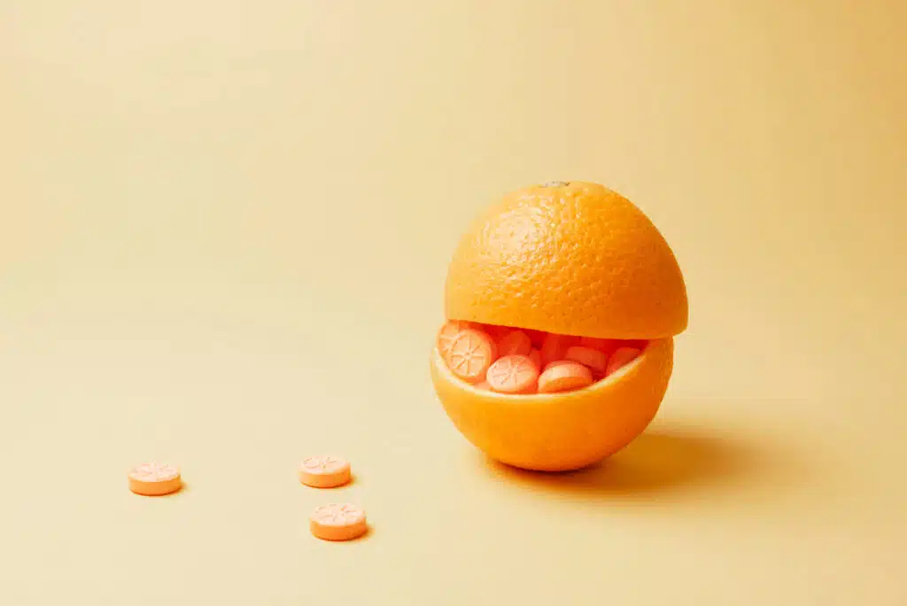 Orange stuffed with orange pills on yellow background. Vitamin C pills as an alternative to citrus fruits. Immune booster concept.