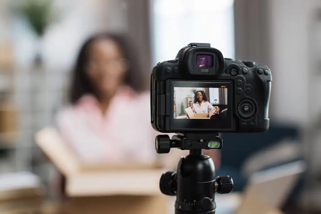 African american woman unboxing parcel with ordered goods while sitting at home and recording video blog. Female influencer using modern digital camera for creating new content.