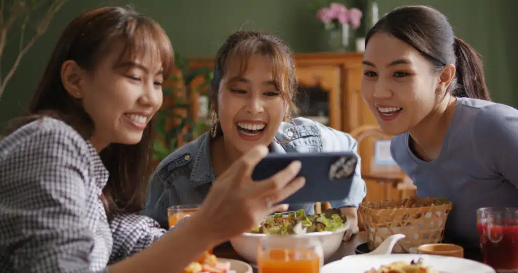 Asia teen girl vlogger group look camera VoIP talk on reel IG tiktok app filming shoot live share vlog. Gen Z youth people enjoy food dinner lunch at reopen cafe with fun joy party laugh relax smile.