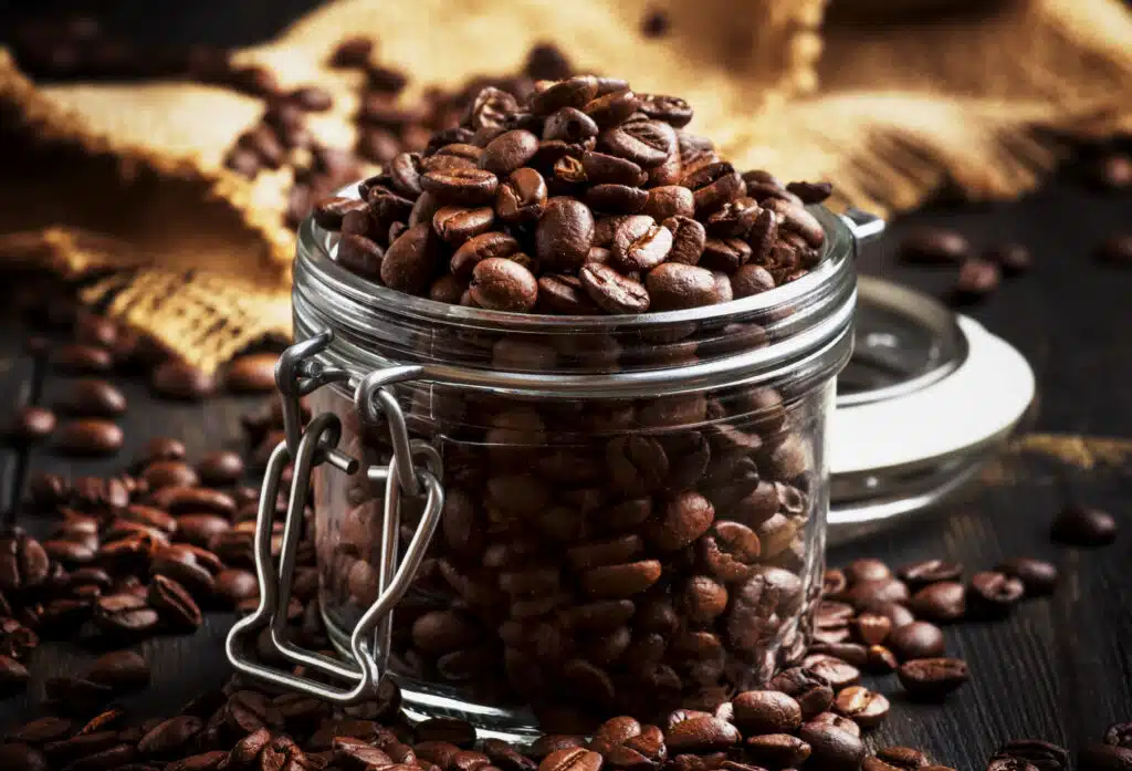 Coffee beans in glass jar, black rustic kitchen table background, selective focus