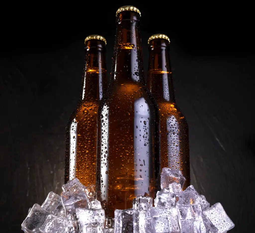 Cold beer with water drops, beer bottles with ice cubes in front of black wooden background
