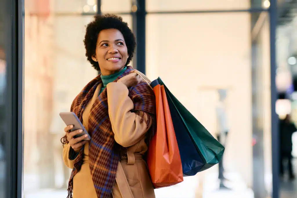 Happy African American woman texting on cell phone while shopping in the city and looking away. Copy space.
