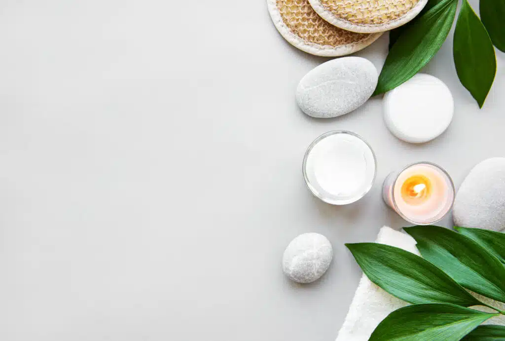 Spa concept, green leaves, candles and moisturizer cream on white background. Flat lay
