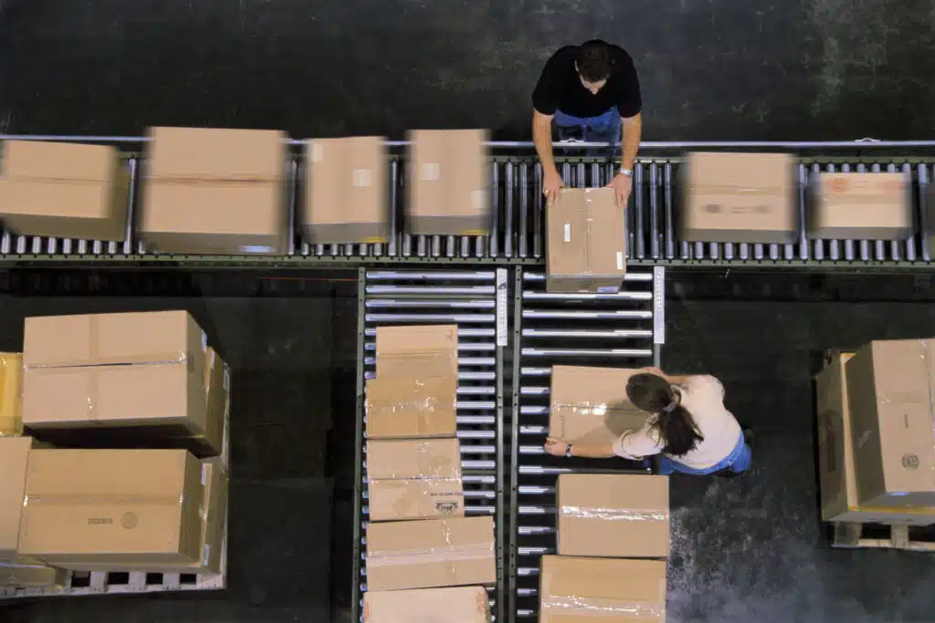 Warehouse employees organizing cardboard boxes moving on a conveyor belt in a distribution warehouse.