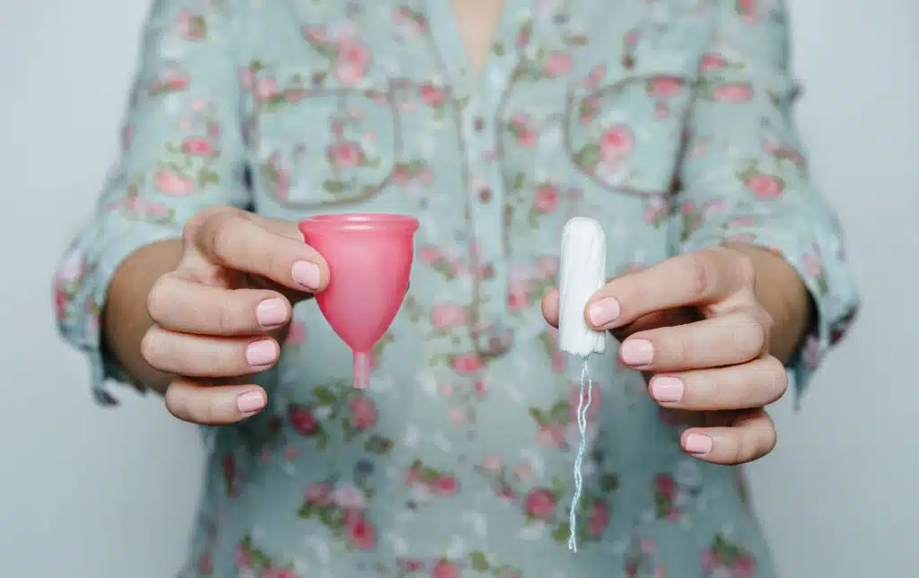 Close up of woman hands comparing menstrual cup and tampon. Concept of different methods of female intimate hygiene.