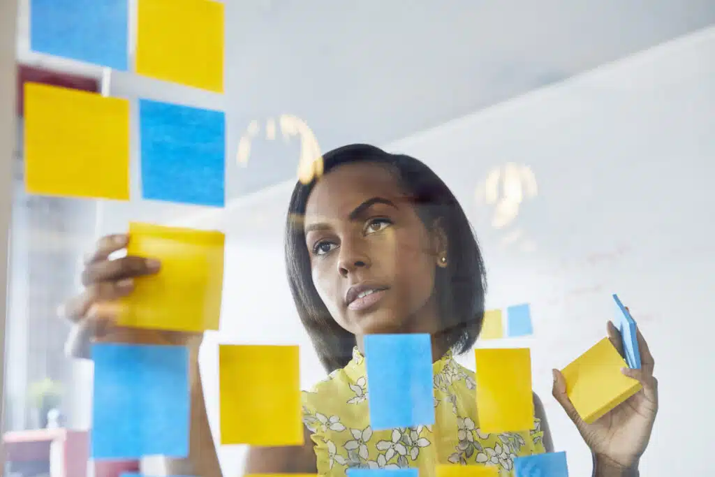 Young woman in office, sticking sticky notes to glass in office