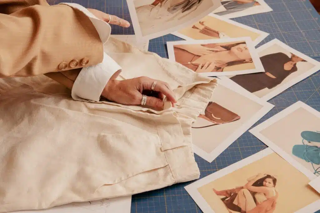 A focused woman, with fashion sketches and fabric swatches spread before her, meticulously planning a clothing line, showcasing the creative process behind a fashion brand's collection.