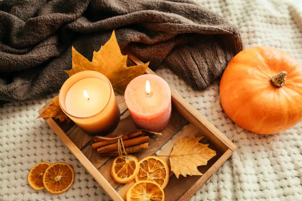 Autumn cozy composition of a knitted sweater and autumn home decor. Candles, fallen leaves, pumpkin and cinnamon sticks to set the mood. Autumn mood.