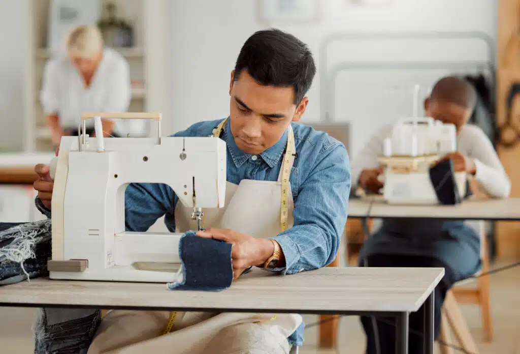 Creative fashion designer learning sewing skills on denim clothes in a clothing manufacturing facto.