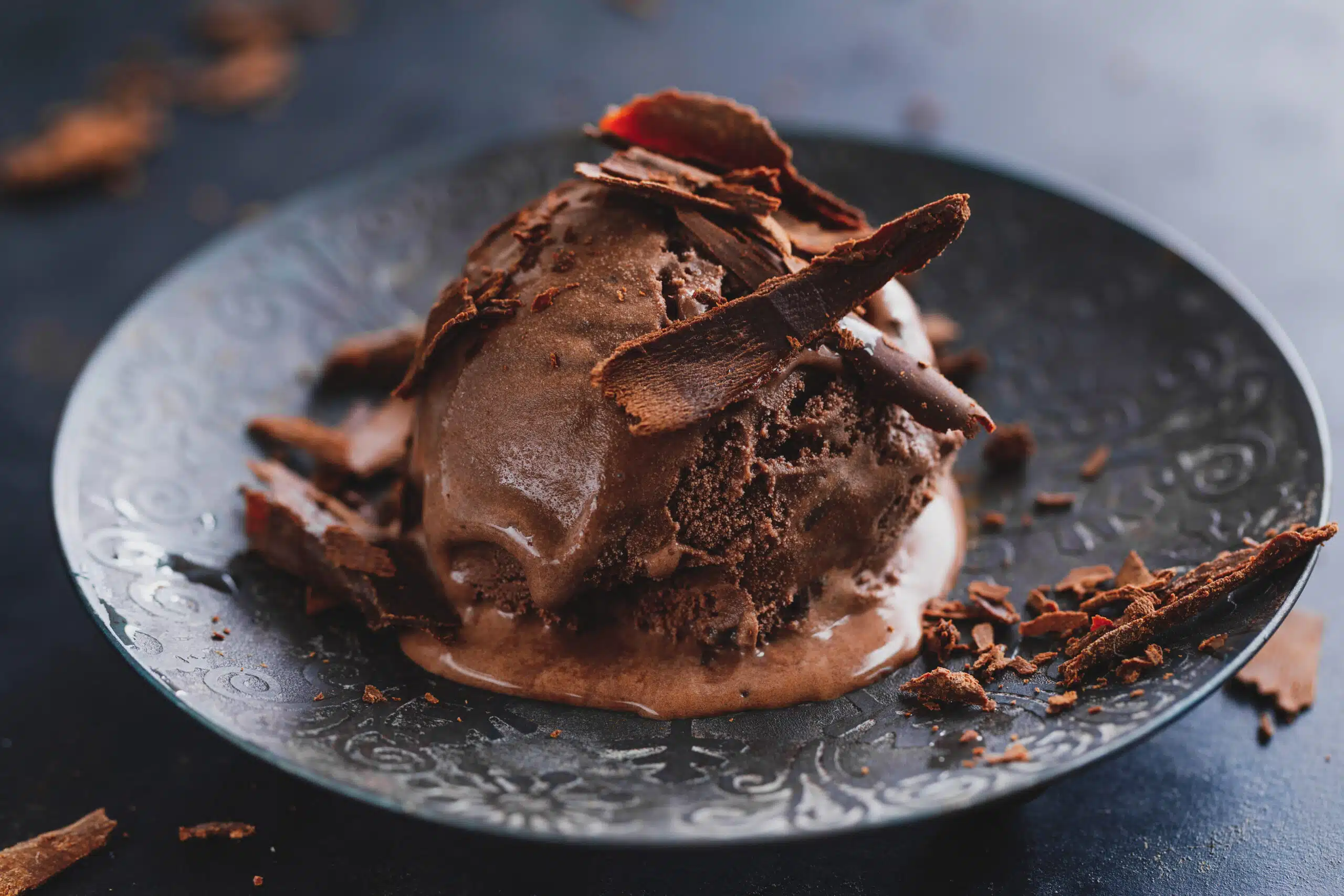 Tasty appetizing chocolate ice cream with chocolate chunks on dark plate on dark background.