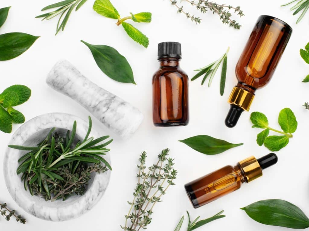Dropper bottles with oil and mortar with herbs on white table flat lay view. Herbal cosmetics concept