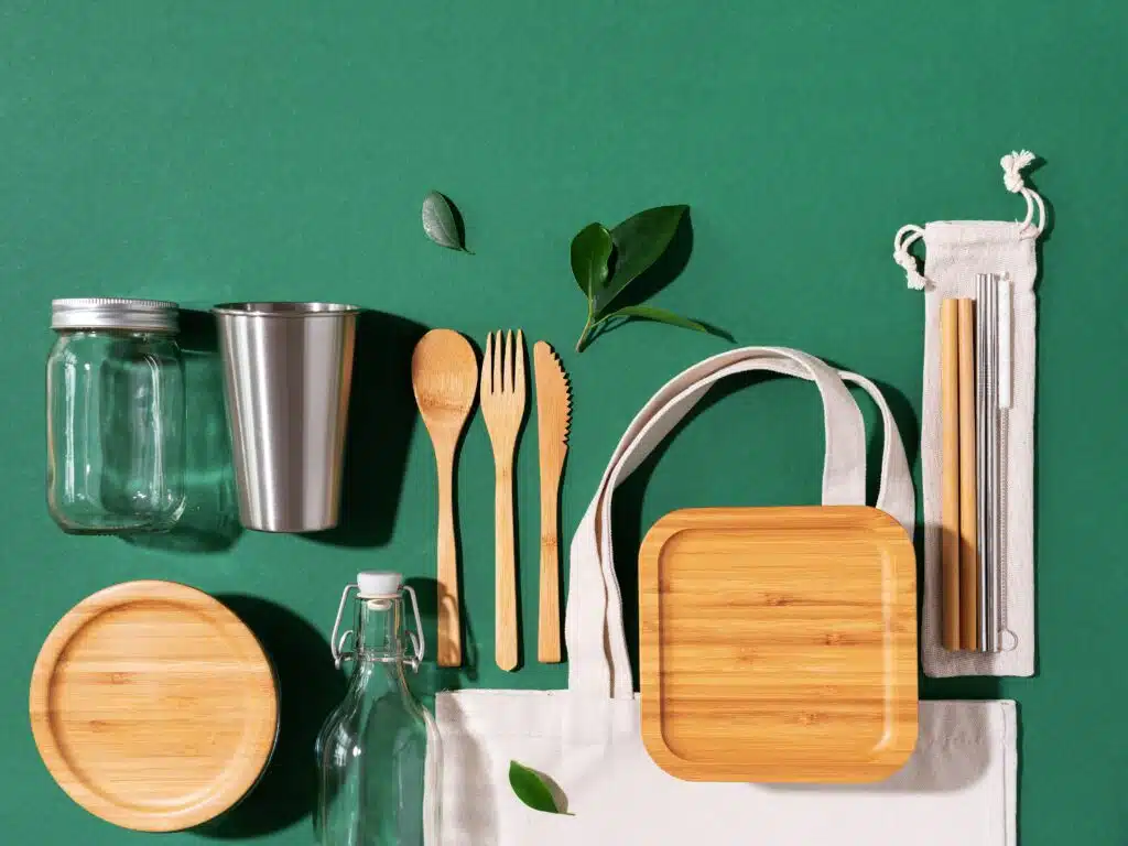 Sustainable lifestyle. Zero waste, plastic free shopping concept. Cotton bags, glass jar, bottle, metal cup, straws for drinking, bamboo cutlery and boxes on green background
