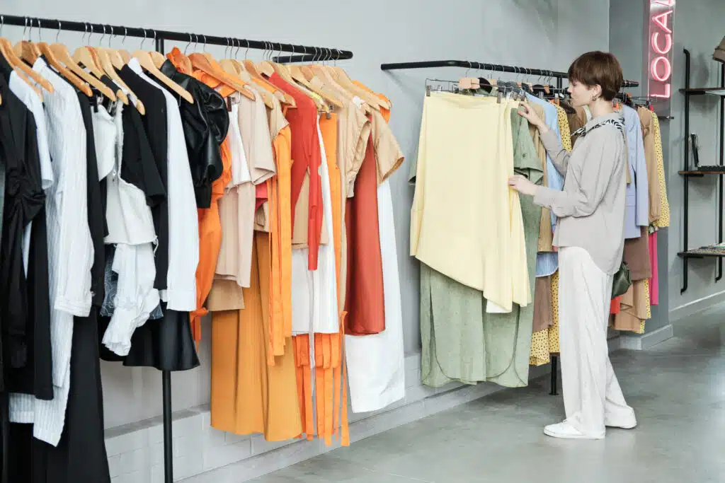 Young woman standing near the rack and choosing new clothes for herself in the showroom